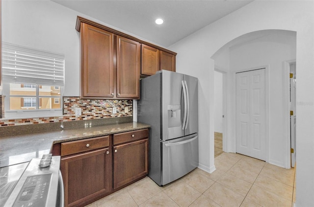5030 Herring Ct, New Port Richey, FL 34652 - kitchen featuring stainless steel fridge with ice dispenser, arched walkways, decorative backsplash, light tile patterned floors, and dark stone counters