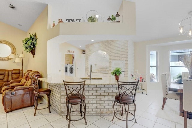 7101 Bucks Ford Dr, Riverview, FL 33578 - kitchen with washer and dryer, light tile patterned floors, a kitchen breakfast bar, light stone counters, and high vaulted ceiling