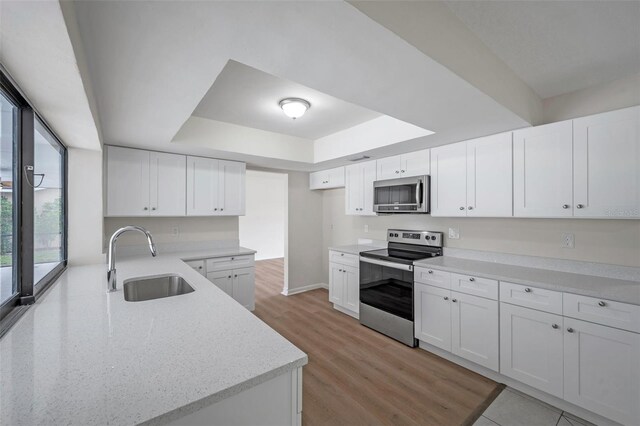 734 Flamingo Dr, Apollo Beach, FL 33572 - kitchen with appliances with stainless steel finishes, a tray ceiling, light stone counters, white cabinets, and light wood-style flooring