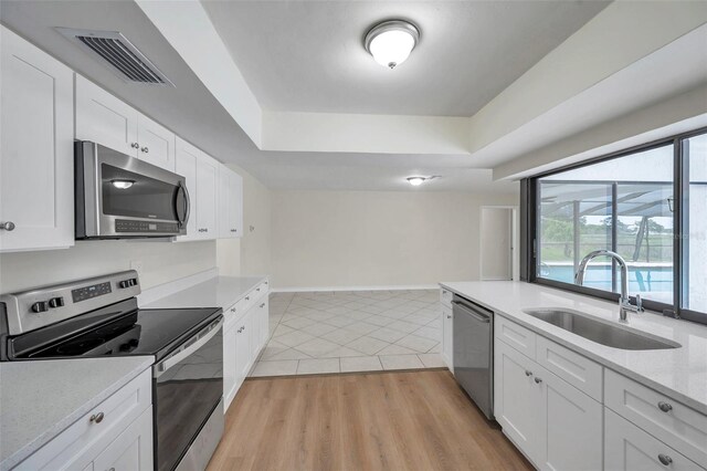 734 Flamingo Dr, Apollo Beach, FL 33572 - kitchen with stainless steel appliances, a tray ceiling, white cabinetry, and light tile patterned floors