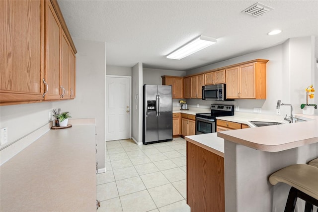 17509 Queensland St, Land O Lakes, FL 34638 - kitchen featuring appliances with stainless steel finishes, light countertops, a kitchen bar, a peninsula, and a textured ceiling