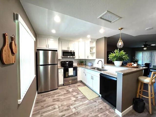 940 Virginia St Unit 303, Dunedin, FL 34698 - kitchen featuring stainless steel appliances, a peninsula, light stone countertops, white cabinets, and light wood-type flooring