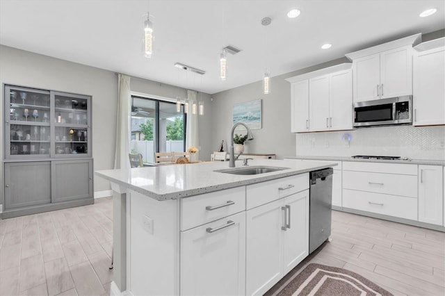 12382 Tibbetts St, Odessa, FL 33556 - kitchen featuring appliances with stainless steel finishes, light wood-style flooring, a center island with sink, decorative backsplash, and light stone countertops