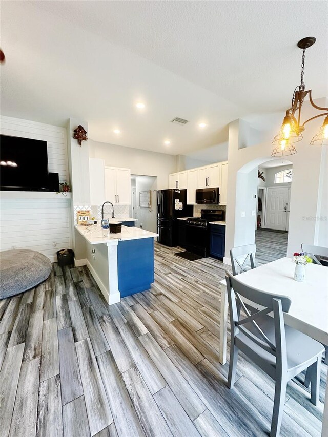 19743 Ellendale Dr, Land O Lakes, FL 34638 - kitchen with black appliances, a peninsula, arched walkways, light wood-style floors, and recessed lighting