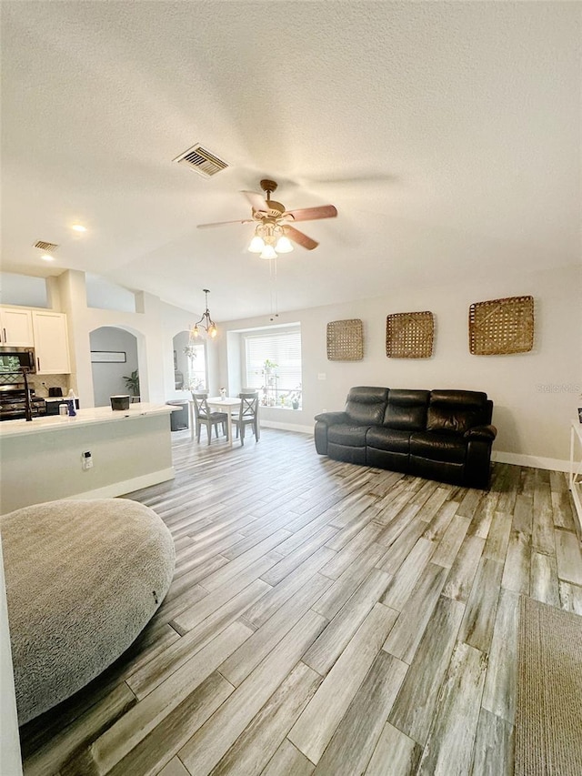 19743 Ellendale Dr, Land O Lakes, FL 34638 - living area with arched walkways, light wood finished floors, ceiling fan, and a textured ceiling