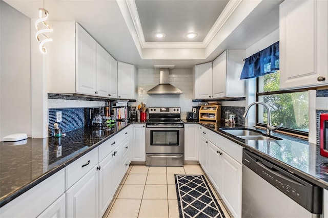 1304 Cedar Ct, Tarpon Springs, FL 34689 - kitchen featuring stainless steel appliances, wall chimney exhaust hood, a tray ceiling, white cabinetry, and crown molding