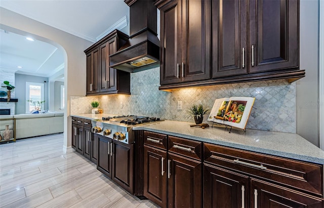 29038 Picana Ln, Wesley Chapel, FL 33543 - kitchen with stainless steel gas cooktop, custom range hood, arched walkways, light stone countertops, and ornamental molding