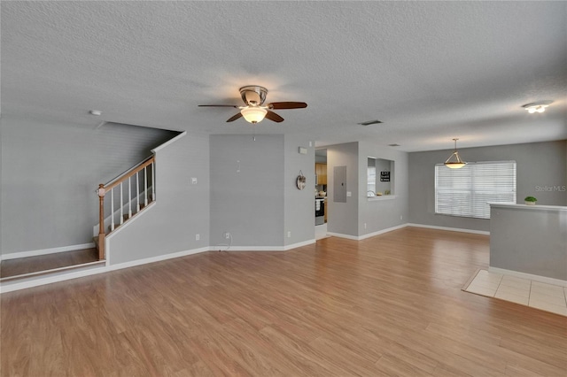 3455 Castle Stone Ct, Valrico, FL 33594 - unfurnished living room featuring ceiling fan, light wood finished floors, a textured ceiling, and stairway