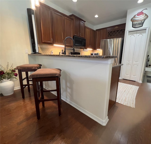 1247 Gentilly Ln, Wesley Chapel, FL 33544 - kitchen featuring dark stone countertops, black microwave, dark wood-type flooring, backsplash, and recessed lighting