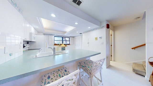 12132 Capri Cir S, Treasure Island, FL 33706 - kitchen with white appliances, a peninsula, a kitchen breakfast bar, white cabinetry, and light countertops