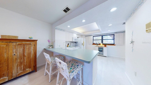 12132 Capri Cir S, Treasure Island, FL 33706 - kitchen featuring white appliances, light wood-style flooring, recessed lighting, a peninsula, and white cabinets