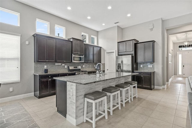 7114 Bowspirit Pl, Apollo Beach, FL 33572 - kitchen featuring appliances with stainless steel finishes, light tile patterned flooring, decorative backsplash, a kitchen breakfast bar, and light stone counters