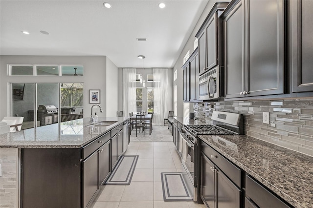 7114 Bowspirit Pl, Apollo Beach, FL 33572 - kitchen featuring appliances with stainless steel finishes, decorative backsplash, a center island with sink, dark stone countertops, and light tile patterned floors