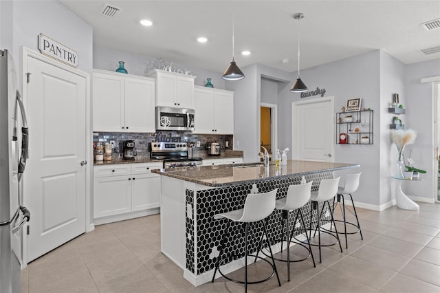 13301 Waterleaf Garden Cir, Riverview, FL 33579 - kitchen featuring stainless steel appliances, light tile patterned floors, decorative backsplash, dark stone countertops, and a breakfast bar