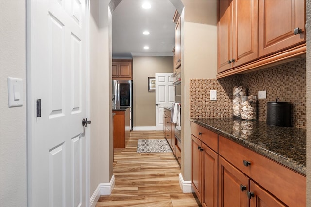 165 Mobbly Bay Dr, Oldsmar, FL 34677 - kitchen featuring light wood-type flooring, decorative backsplash, brown cabinetry, dark stone countertops, and crown molding