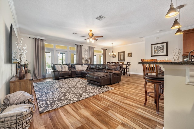 165 Mobbly Bay Dr, Oldsmar, FL 34677 - living area featuring a ceiling fan, light wood finished floors, crown molding, a textured ceiling, and a chandelier