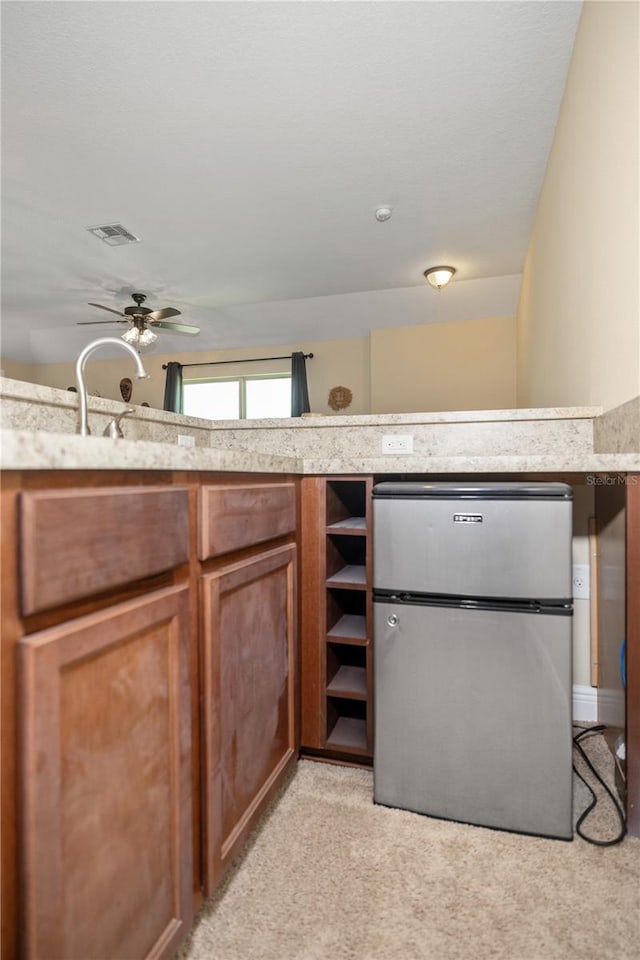 165 Mobbly Bay Dr, Oldsmar, FL 34677 - kitchen with freestanding refrigerator, light colored carpet, ceiling fan, and brown cabinets