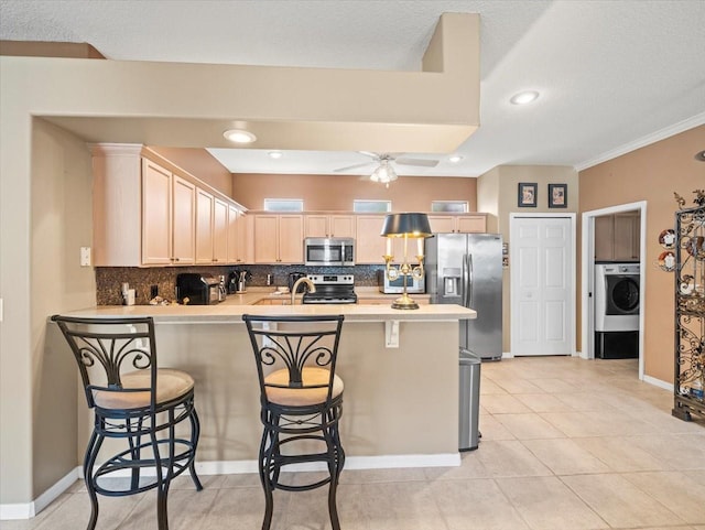7606 Berna Ln, Land O Lakes, FL 34637 - kitchen featuring appliances with stainless steel finishes, washer / dryer, a peninsula, backsplash, and light brown cabinetry