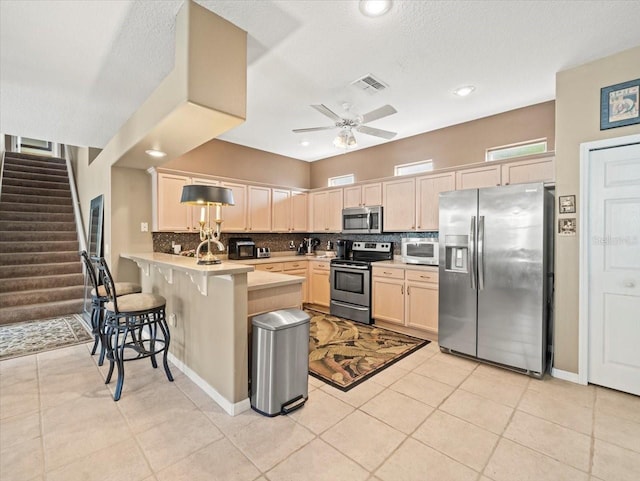 7606 Berna Ln, Land O Lakes, FL 34637 - kitchen with appliances with stainless steel finishes, a peninsula, decorative backsplash, light countertops, and light brown cabinetry