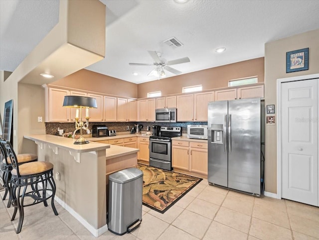 7606 Berna Ln, Land O Lakes, FL 34637 - kitchen with stainless steel appliances, a peninsula, light brown cabinetry, tasteful backsplash, and light countertops