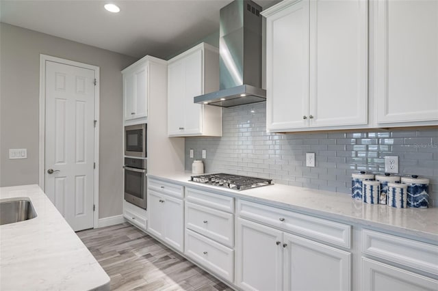 12652 Shetland Walk Dr, Lithia, FL 33547 - kitchen featuring wall chimney range hood, appliances with stainless steel finishes, white cabinetry, light stone countertops, and backsplash