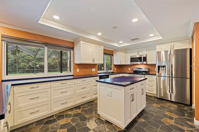 10053 W Bay St, Seminole, FL 33776 - kitchen with appliances with stainless steel finishes, a tray ceiling, ornamental molding, dark countertops, and a center island