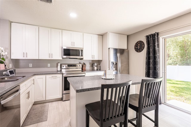 4132 Festival Pointe Blvd, Mulberry, FL 33860 - kitchen featuring stainless steel appliances, a kitchen bar, white cabinets, a kitchen island, and dark stone countertops