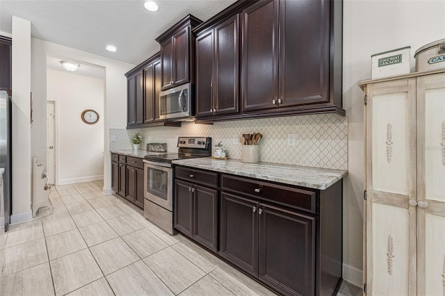 1237 Windy Bay Shl, Tarpon Springs, FL 34689 - kitchen with appliances with stainless steel finishes, tasteful backsplash, dark brown cabinets, light stone counters, and light tile patterned floors