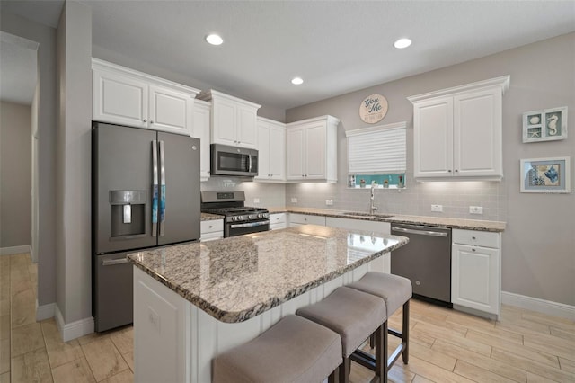 6408 Seasound Dr, Apollo Beach, FL 33572 - kitchen featuring stainless steel appliances, a kitchen island, white cabinets, tasteful backsplash, and light stone countertops