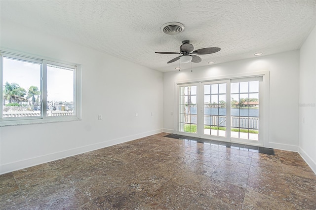 5950 Bikini Way N, St Pete Beach, FL 33706 - empty room with ceiling fan, a water view, a textured ceiling, recessed lighting, and stone finish floors