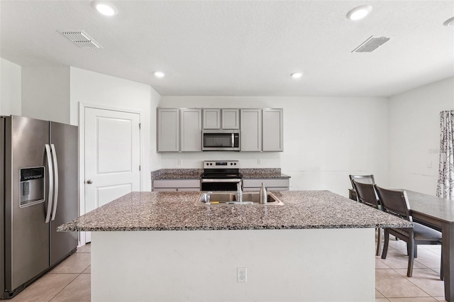33657 Field Maple Loop, Wesley Chapel, FL 33545 - kitchen featuring stainless steel appliances, gray cabinets, light tile patterned flooring, a kitchen island with sink, and dark stone counters