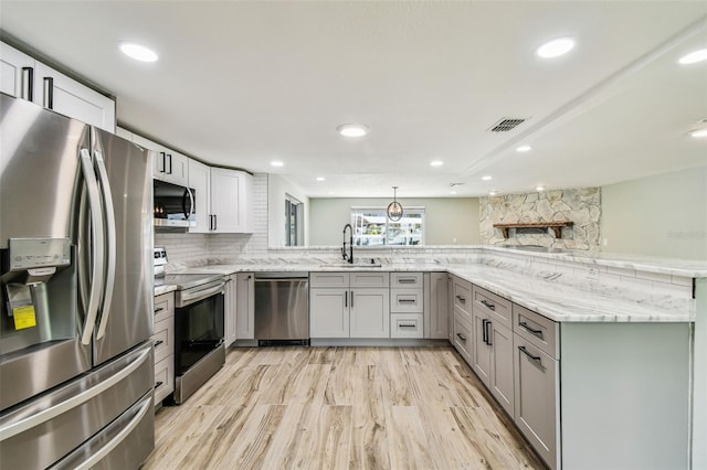 13909 Berkowitz Ave, Hudson, FL 34667 - kitchen with stainless steel appliances, gray cabinets, a peninsula, light stone counters, and backsplash