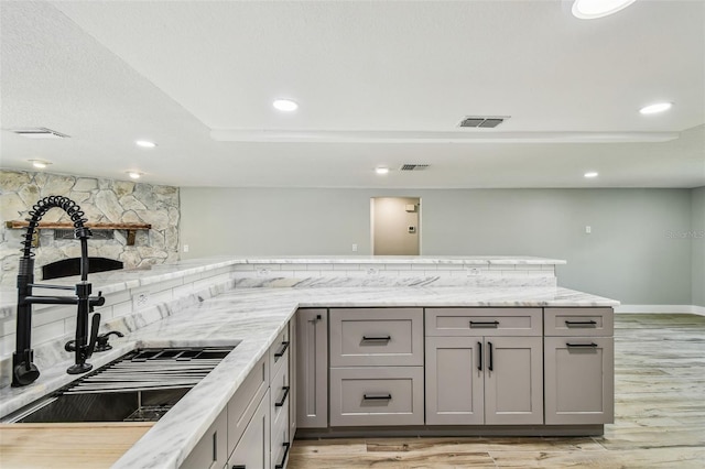 13909 Berkowitz Ave, Hudson, FL 34667 - kitchen featuring gray cabinets, light wood-type flooring, a stone fireplace, recessed lighting, and decorative backsplash