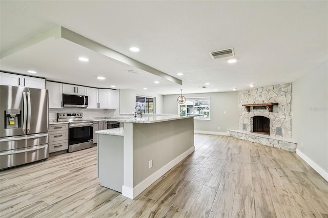 13909 Berkowitz Ave, Hudson, FL 34667 - kitchen with stainless steel appliances, light wood-type flooring, light stone countertops, white cabinets, and tasteful backsplash