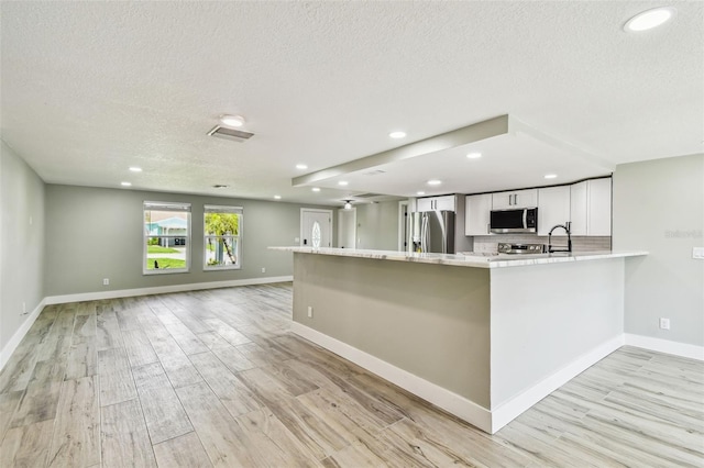 13909 Berkowitz Ave, Hudson, FL 34667 - kitchen featuring stainless steel appliances, a textured ceiling, recessed lighting, light wood-style flooring, and white cabinets