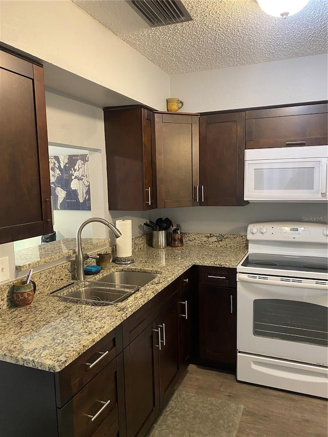 832 Cambridge Ct, Dunedin, FL 34698 - kitchen with white appliances, a textured ceiling, light wood-type flooring, light stone countertops, and dark brown cabinets