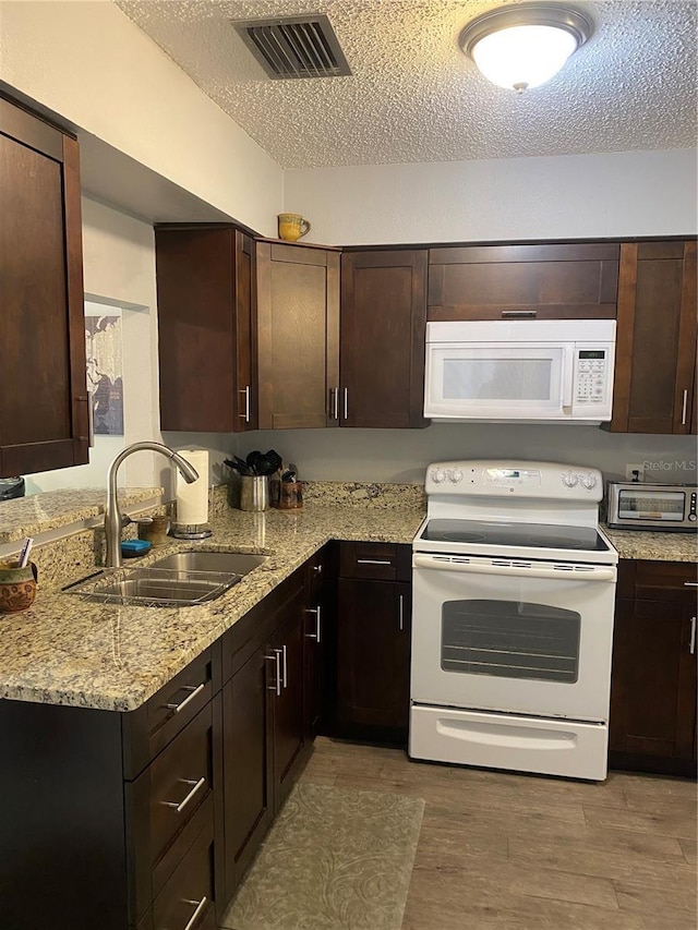 832 Cambridge Ct, Dunedin, FL 34698 - kitchen with white appliances, a textured ceiling, dark brown cabinets, light stone countertops, and light wood finished floors