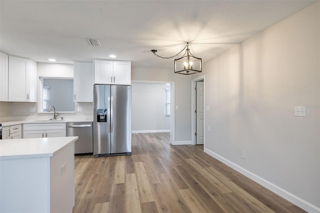 314 Circle Dr, Palm Harbor, FL 34683 - kitchen featuring appliances with stainless steel finishes, white cabinetry, light countertops, a chandelier, and light wood-style flooring