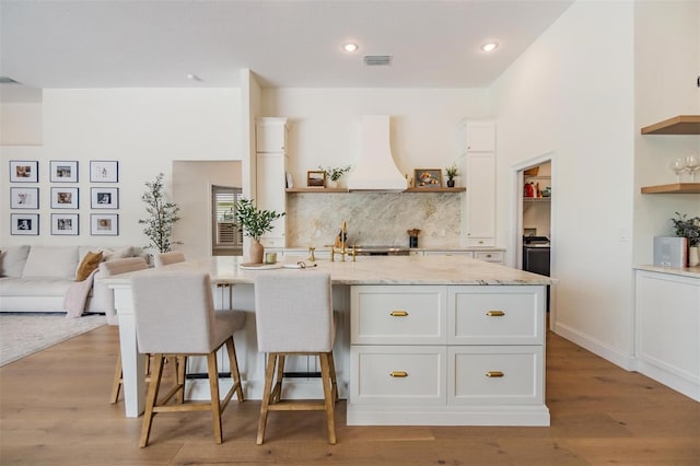 9126 Cypress Keep Ln, Odessa, FL 33556 - kitchen with open shelves, custom range hood, white cabinets, light stone countertops, and a breakfast bar area