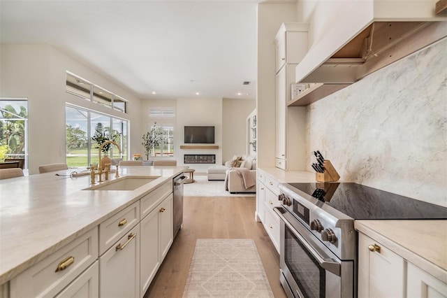 9126 Cypress Keep Ln, Odessa, FL 33556 - kitchen featuring appliances with stainless steel finishes, custom exhaust hood, light wood-type flooring, a glass covered fireplace, and recessed lighting