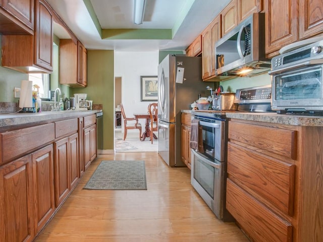 1610 Sanderling Ct, Brandon, FL 33511 - kitchen featuring appliances with stainless steel finishes, a tray ceiling, light wood-style floors, and brown cabinetry