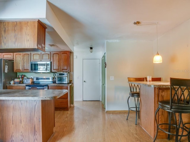 1610 Sanderling Ct, Brandon, FL 33511 - kitchen with stainless steel appliances, a breakfast bar, light wood finished floors, brown cabinetry, and pendant lighting