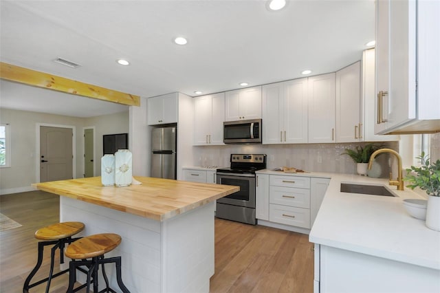 245 Grove Cir N, Dunedin, FL 34698 - kitchen featuring stainless steel appliances, a kitchen breakfast bar, light wood-type flooring, white cabinetry, and recessed lighting