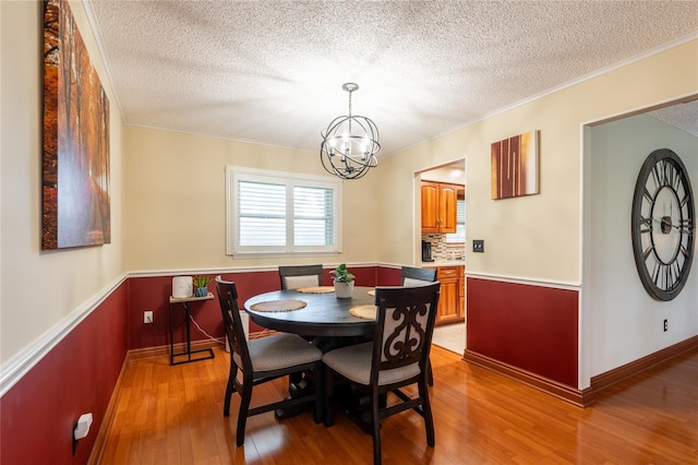 616 Pawn Way, Seffner, FL 33584 - dining room featuring a textured ceiling, a chandelier, light wood finished floors, ornamental molding, and a wainscoted wall