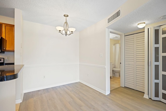 302 Lake Parsons Grn Unit 104, Brandon, FL 33511 - unfurnished dining area with light wood-style flooring, a chandelier, and a textured ceiling