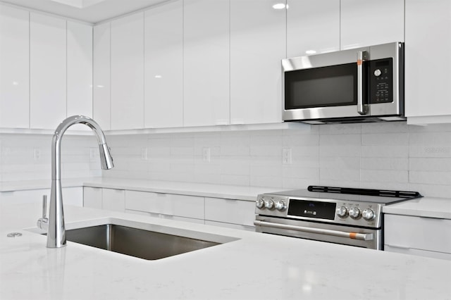 400 150th Ave Unit 205, Madeira Beach, FL 33708 - kitchen featuring appliances with stainless steel finishes, modern cabinets, white cabinetry, decorative backsplash, and light stone counters