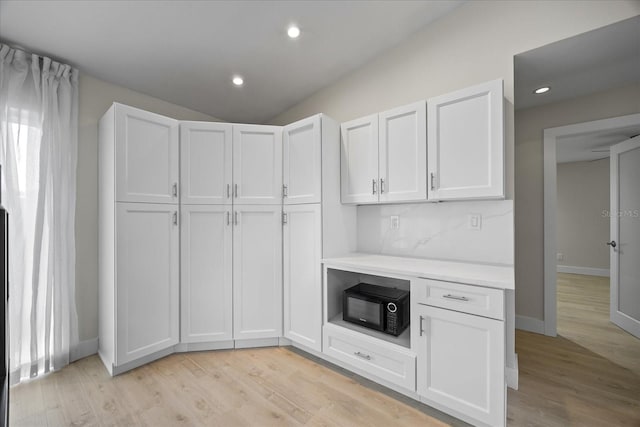 3956 Versailles Dr, Tampa, FL 33634 - kitchen featuring black microwave, light countertops, white cabinets, light wood-style floors, and vaulted ceiling