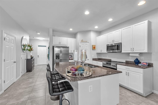 7124 Summer Holly Pl, Riverview, FL 33578 - kitchen featuring appliances with stainless steel finishes, dark stone countertops, light tile patterned floors, a breakfast bar area, and white cabinets
