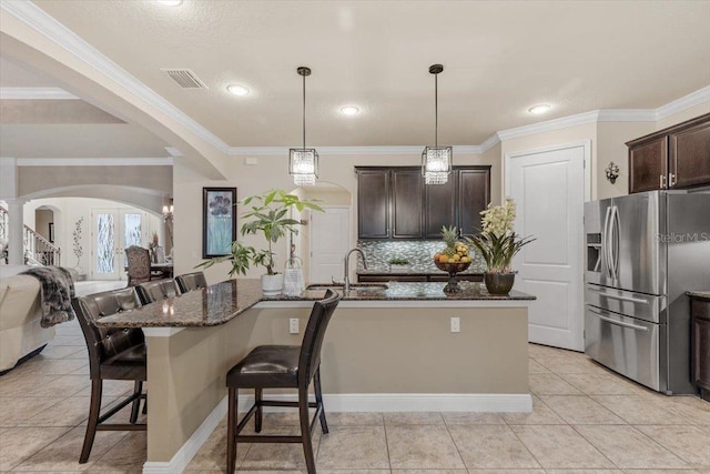 8358 Dunham Station Dr, Tampa, FL 33647 - kitchen with stainless steel refrigerator with ice dispenser, a breakfast bar area, dark stone counters, dark brown cabinetry, and crown molding
