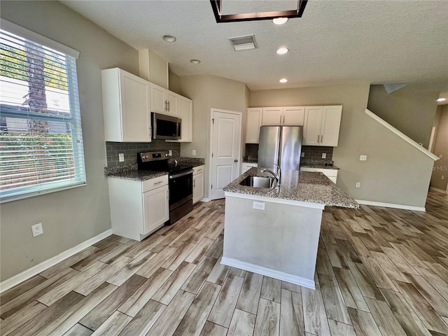 2612 E 26th Ave, Tampa, FL 33605 - kitchen featuring appliances with stainless steel finishes, light wood finished floors, decorative backsplash, white cabinets, and a textured ceiling